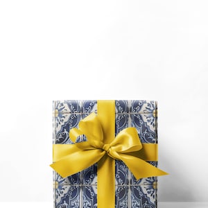 May include: A wrapped gift box with a blue and white tile pattern, tied with a bright yellow satin ribbon and bow. The gift box is rectangular and sits against a white background.