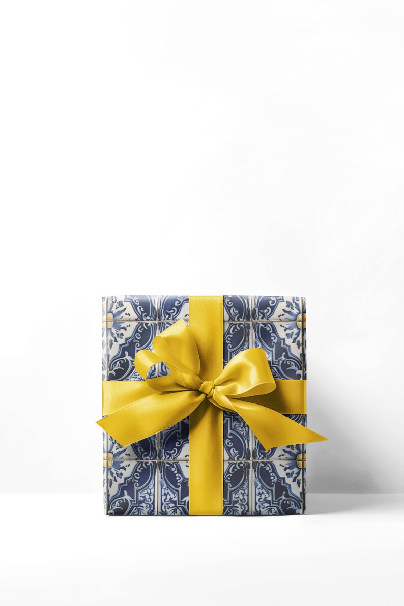 May include: A wrapped gift box with a blue and white tile pattern, tied with a bright yellow satin ribbon and bow. The gift box is rectangular and sits against a white background.
