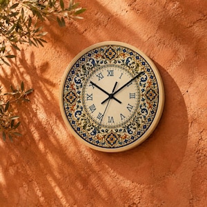 May include: A round wall clock featuring a cream-colored face with black Roman numerals and black hands. The border displays a decorative pattern in shades of blue, yellow, and orange, with intricate floral and geometric motifs surrounding the dial.