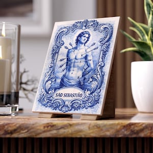 May include: A blue and white decorative tile featuring an illustration of a man with arrows, framed by ornate scrollwork. The tile is propped up on a wooden stand and has the text "SÃO SEBASTIÃO".