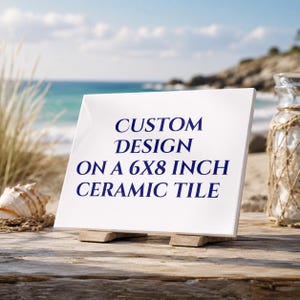 May include: A white ceramic tile with the text "CUSTOM DESIGN ON A 6X8 INCH CERAMIC TILE" in navy blue. The tile is displayed on a wooden stand, with a beach scene in the background.