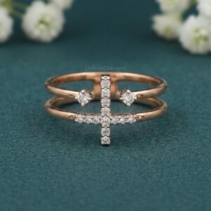 May include: Rose gold ring with a double band design. The ring features a cross-shaped arrangement of small, sparkling diamonds in the center. Two square-shaped diamonds are set on either side of the cross, adding to the ring's elegant appearance.