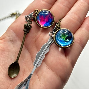 May include: Two silver spoons with a feather and crown design, and two glass pendants with a galaxy and earth image.