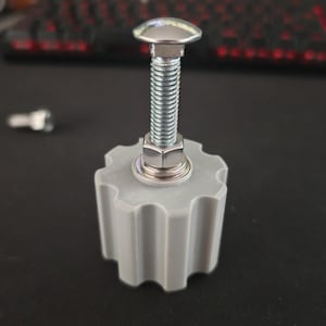 Puede incluir: Un pomo gris en forma de engranaje con un perno y una tuerca metálicos. El perno tiene una cabeza plateada y redondeada. El pomo está hecho de un material gris claro y tiene un borde acanalado.