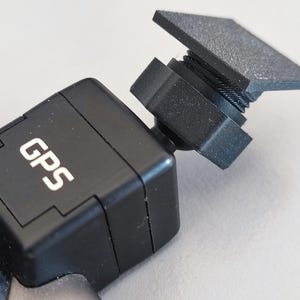 Può includere: Un dispositivo GPS nero con le lettere "GPS" in bianco. Il dispositivo ha una forma quadrata con una parte superiore rettangolare e una vite filettata. Il dispositivo è realizzato in un materiale strutturato.