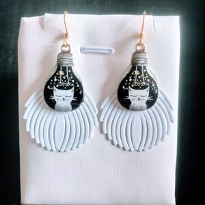 Grote oorbellen met kattenmotief, witte lakverenprint en geëmailleerde bolvormige hanger met afbeelding van een kat.