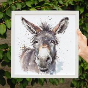 May include: A watercolour painting of a donkey with a friendly expression. The donkey is grey and brown with a white muzzle and large ears. The background is white with splashes of blue and gold paint.