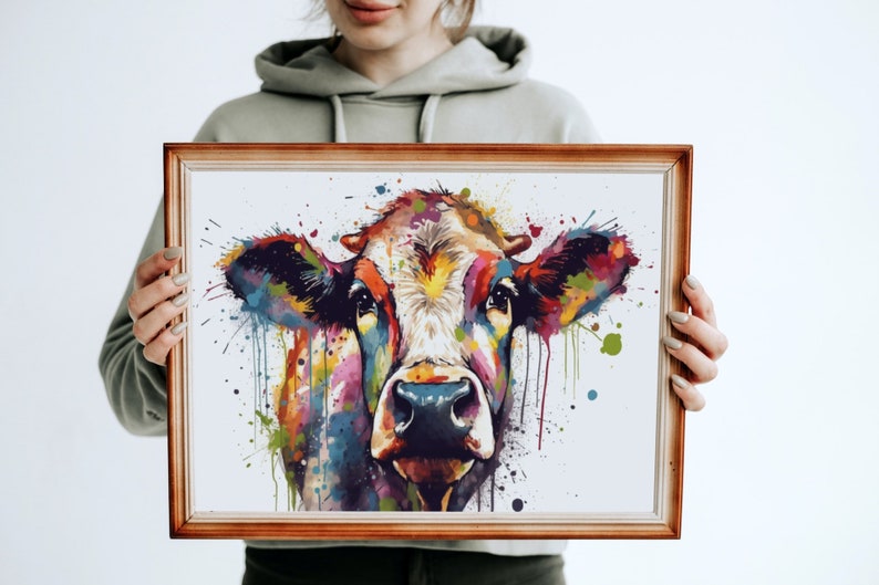 May include: A framed watercolor painting of a cow's head with colorful splashes of paint. The cow's face is mostly white with brown spots and the background is white.