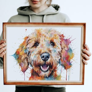 May include: A watercolor painting of a dog's face with colorful splashes of paint. The dog is a light brown color with a happy expression. The painting is framed in a simple wooden frame.