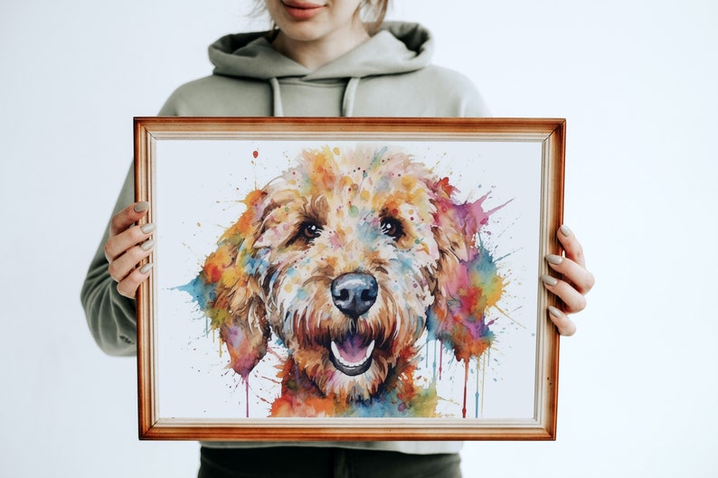 May include: A watercolor painting of a dog's face with colorful splashes of paint. The dog is a light brown color with a happy expression. The painting is framed in a simple wooden frame.