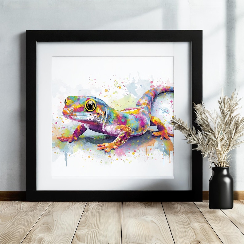 May include: A framed watercolor print of a gecko in vibrant colors. The gecko is depicted with a rainbow of hues, including yellow, blue, pink, and orange. The artwork is framed in a black square frame, adding a modern touch to the colorful reptile.