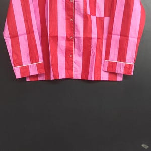 K&ouml;nnte beinhalten: Ein lang&auml;rmliges Hemd mit rosa und roten Streifen, einer wei&szlig;en Knopfleiste und einem wei&szlig;en Besatz an Kragen und &Auml;rmelb&uuml;ndchen.