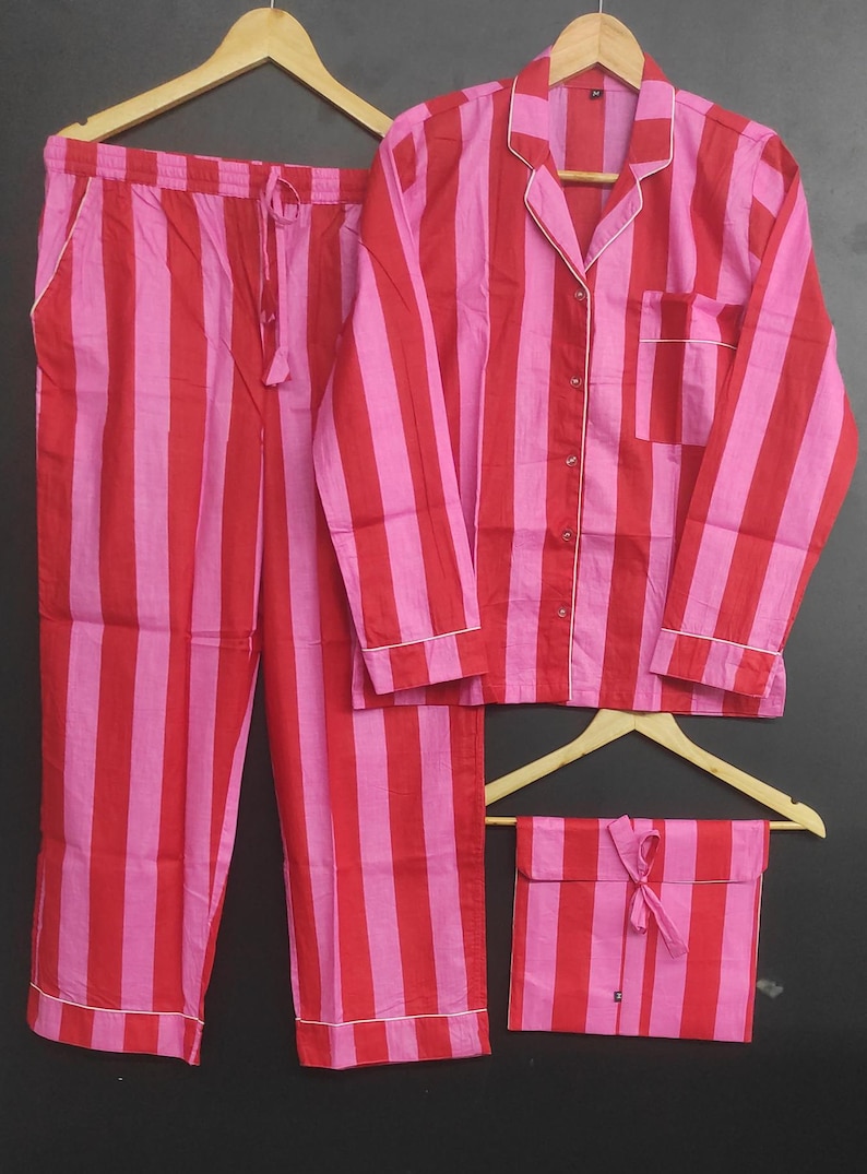 K&ouml;nnte beinhalten: Ein gestreiftes Pyjama-Set mit einem lang&auml;rmeligen Hemd und einer Hose. Das Set ist rosa und rot mit wei&szlig;en Verzierungen. Eine passende gestreifte Tasche ist im Lieferumfang enthalten.