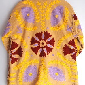 May include: A tan quilted jacket with a brown faux fur collar. The jacket is embroidered with yellow, purple, and red floral designs.