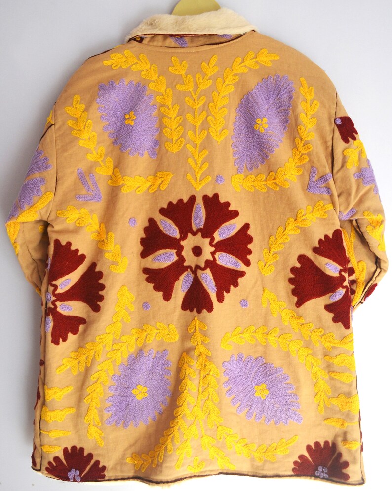 May include: A tan quilted jacket with a brown faux fur collar. The jacket is embroidered with yellow, purple, and red floral designs.