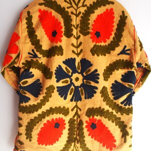 May include: A tan jacket with a faux fur collar and intricate embroidery. The embroidery features red, blue, and green floral patterns.