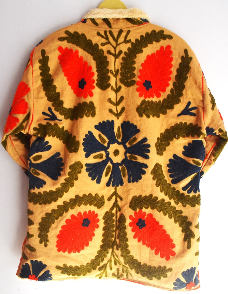 May include: A tan jacket with a faux fur collar and intricate embroidery. The embroidery features red, blue, and green floral patterns.