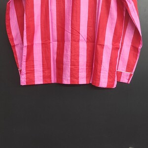 K&ouml;nnte beinhalten: Ein lang&auml;rmliges Hemd mit vertikalen rosa und roten Streifen. Das Hemd hat einen Knopfkrag und eine lockere Passform.