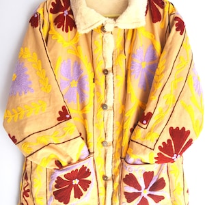 May include: A beige embroidered jacket with a faux fur collar. The jacket features a floral pattern in shades of yellow, purple, and red.