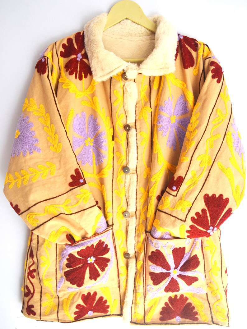 May include: A beige embroidered jacket with a faux fur collar. The jacket features a floral pattern in shades of yellow, purple, and red.
