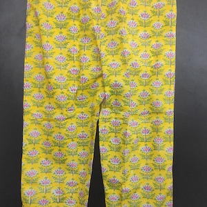Op de afbeelding: Gele pyjamabroek met een herhalend bloemenpatroon in roze, groen en wit. De broek is gemaakt van een lichte stof en heeft een comfortabele, relaxte pasvorm. Het bloemmotief is gelijkmatig verdeeld over het gehele oppervlak.