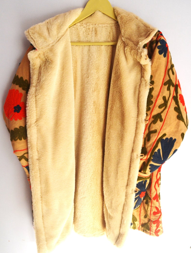 May include: A tan jacket with a floral embroidered design in shades of red, green, blue, and orange. The jacket is lined with a soft, cream-colored faux fur.