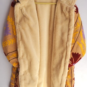 May include: A tan embroidered jacket with a floral pattern in shades of purple, red, and yellow. The jacket is lined with a soft, beige faux fur.