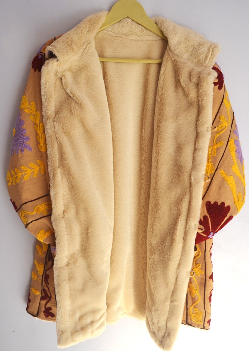 May include: A tan embroidered jacket with a floral pattern in shades of purple, red, and yellow. The jacket is lined with a soft, beige faux fur.