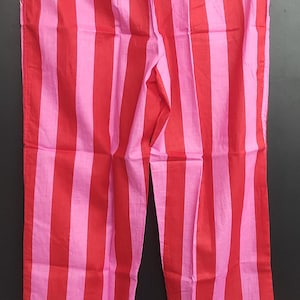 K&ouml;nnte beinhalten: Rote und rosa gestreifte Schlafanzughose mit wei&szlig;em Saum. Die Hose hat einen elastischen Bund.