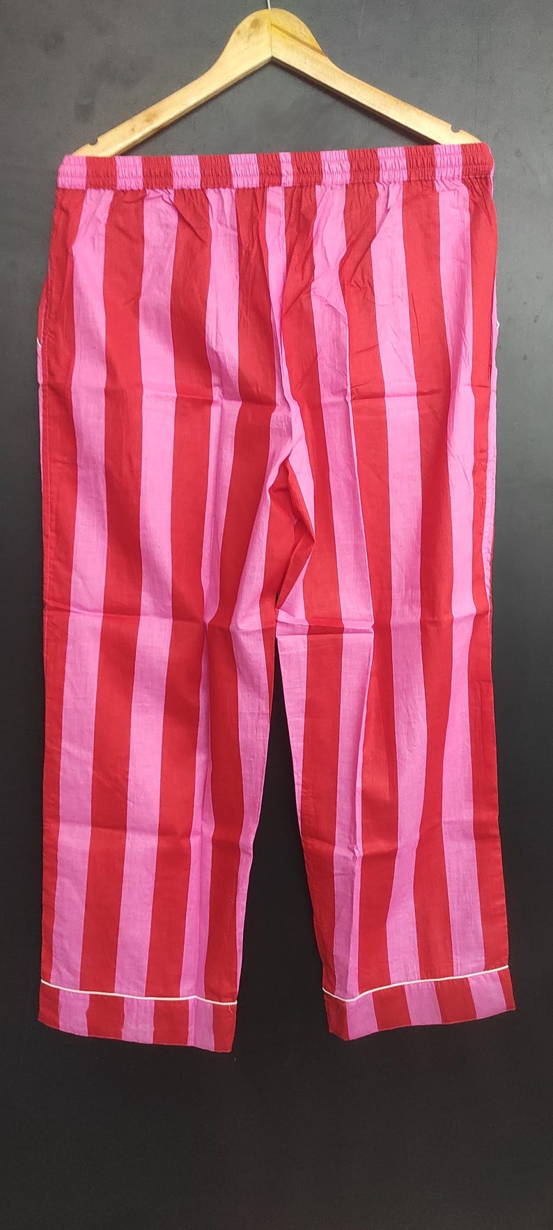 K&ouml;nnte beinhalten: Rote und rosa gestreifte Schlafanzughose mit wei&szlig;em Saum. Die Hose hat einen elastischen Bund.