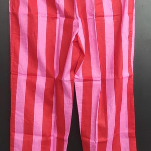 K&ouml;nnte beinhalten: Rote und rosa gestreifte Schlafanzughose mit wei&szlig;em Saum. Die Hose h&auml;ngt an einem Holzb&uuml;gel.