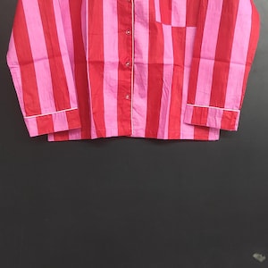 K&ouml;nnte beinhalten: Ein lang&auml;rmliges Hemd mit rosa und roten Streifen, wei&szlig;em Kragen und Knopfleiste.