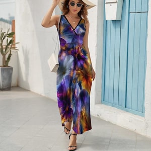 May include: Sleeveless maxi dress with a vibrant floral pattern in shades of purple, blue, orange, and white. The dress features a V-neckline with black trim. The model is wearing black sandals and a straw hat.