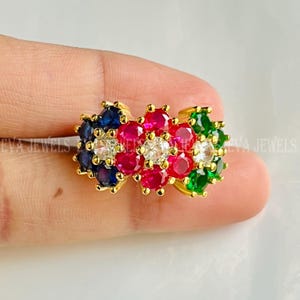 Pode incluir: Um anel de ouro com um design floral adornado com aglomerados de pedras preciosas. O anel apresenta uma vibrante variedade de cores, incluindo pedras azuis, vermelhas, verdes e transparentes. As pedras são engastadas numa banda de ouro.