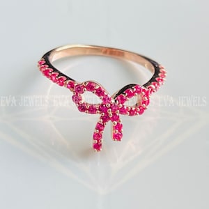 May include: A rose gold ring with a pink bow design. The bow is made of small pink stones and the band is also set with pink stones.