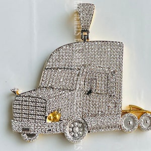 Könnte beinhalten: Ein Anhänger in Form eines silbernen und goldenen Sattelschleppers, der mit funkelnden, klaren Steinen besetzt ist. Der Anhänger ist eine detaillierte Darstellung eines Sattelschleppers mit Fahrerhaus, Anhänger und Rädern.