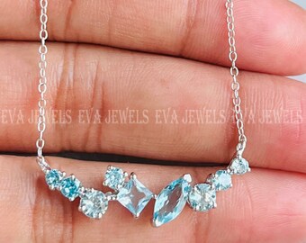 Puede incluir: Un collar de cadena de plata con un diseño delicado que presenta un grupo de piedras preciosas azules. Las piedras preciosas son de varias formas y tamaños, incluyendo redondas, ovaladas y cuadradas.