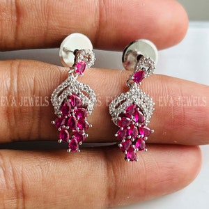 May include: A pair of silver dangle earrings with a cluster of pink gemstones and clear cubic zirconia stones.