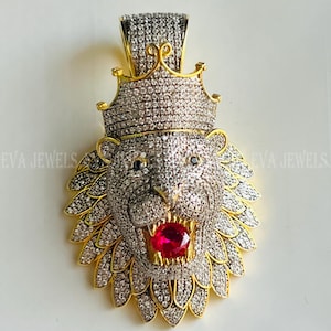 May include: Gold lion head pendant with a crown and red stone in its mouth. The pendant is covered in clear and black stones.