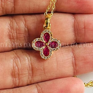 Peut inclure: Un collier pendentif doré avec un motif de trèfle à quatre feuilles. Chaque feuille est une pierre précieuse rouge foncé en forme de goutte d'eau, entourée de petits cristaux transparents. Le collier a une chaîne dorée délicate.