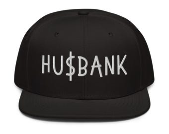 Peut inclure: Casquette de baseball noire avec un motif brodé blanc qui dit "HUS$BANK".