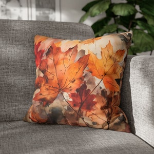 May include: A throw pillow featuring a watercolour design of autumn leaves in shades of orange, red, and brown.