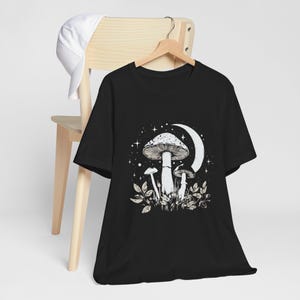 May include: Black t-shirt with a white graphic of mushrooms and a crescent moon with stars.