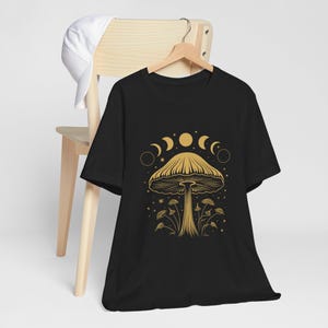 May include: Black t-shirt with a gold outline of a mushroom and moon phases. The text "Shroom Queens" is printed on the shirt.