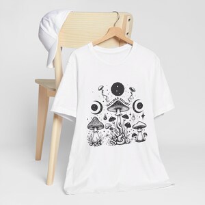 Op de afbeelding: Wit T-shirt met een zwart-witte afbeelding van paddenstoelen en de tekst "Nature's Secret".