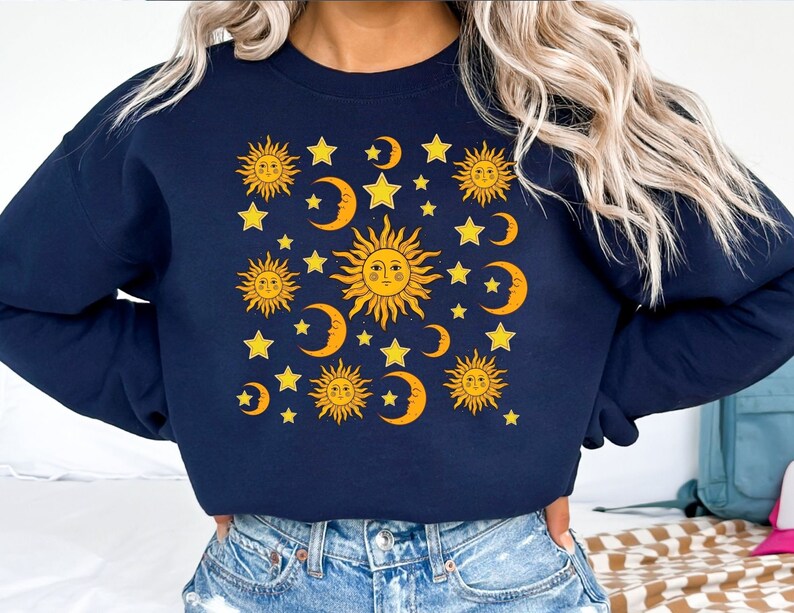 May include: A navy blue sweatshirt with a graphic print of yellow suns, moons, and stars.