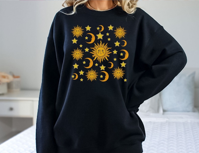 May include: Black sweatshirt with a graphic print of yellow suns and moons with stars on a black background.