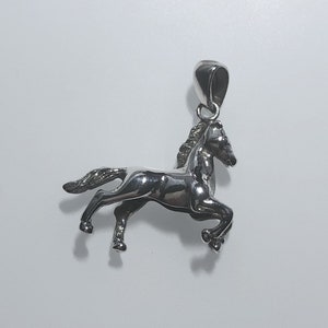 May include: A silver horse pendant charm. The horse is in a running pose with its head turned to the side. The pendant has a loop at the top for attaching to a chain.
