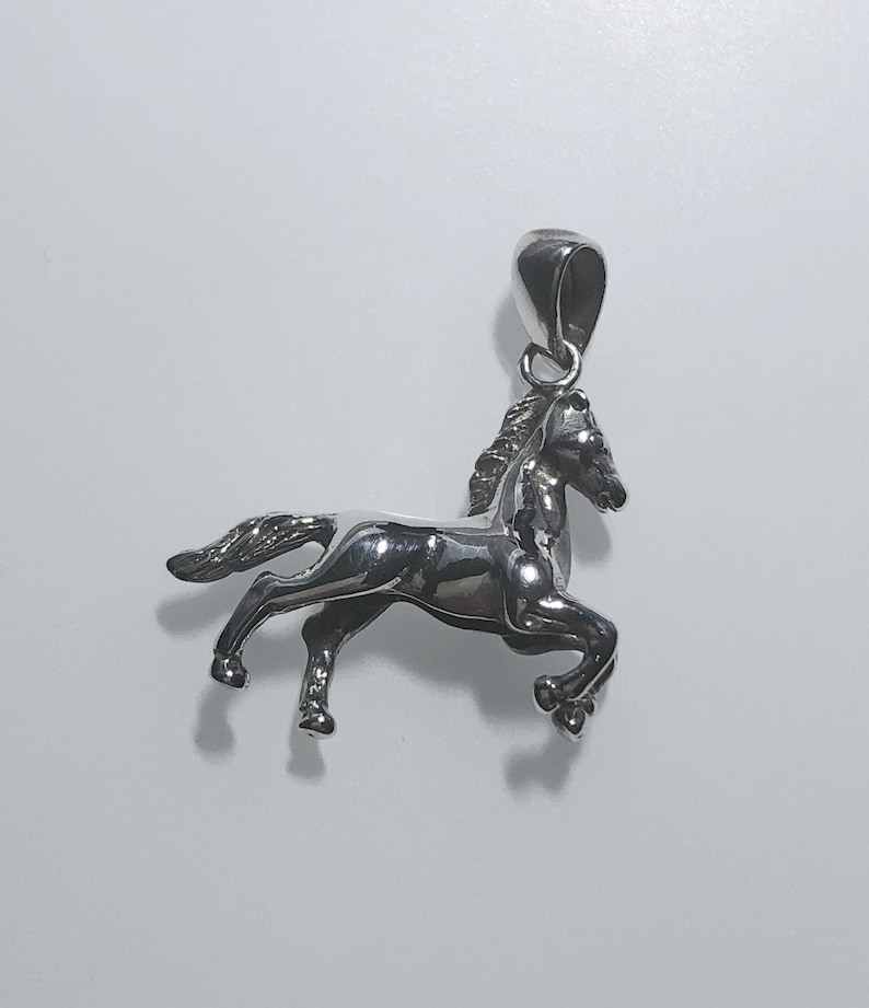 May include: A silver horse pendant charm. The horse is in a running pose with its head turned to the side. The pendant has a loop at the top for attaching to a chain.