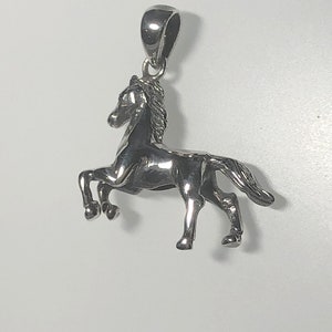 May include: A silver horse pendant charm. The horse is standing on all four legs with its head held high. The pendant has a loop at the top for attaching to a chain or bracelet.